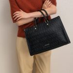 Zdjęcie przedstawiające osobę trzymającą czarną torebkę marki Nine West z monogramem „NW” i widocznym logo.