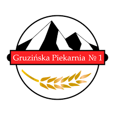 Logo Gruzińskiej Piekarni Nr 1 przedstawiające okrągłą grafikę z wizerunkiem gór, czerwoną wstęgą z białym napisem oraz złotym kłosem zboża w dolnej części.